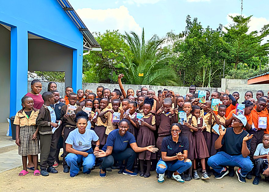 A large group of Zambian schoolchildren holding up their Suku books with the Kulanda House team